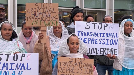 Frauen in traditionell eritreischer Kleidung halten Schilder hoch: "Stop Criminal Human Traficking Network"