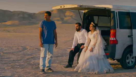 Two men and a woman are sitting and standing in front of a white bus.