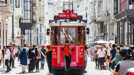 Ein kleiner Junge zeigt den Daumen nach oben, er fährt hinten auf einer roten Tram durch eine belebte Straße.