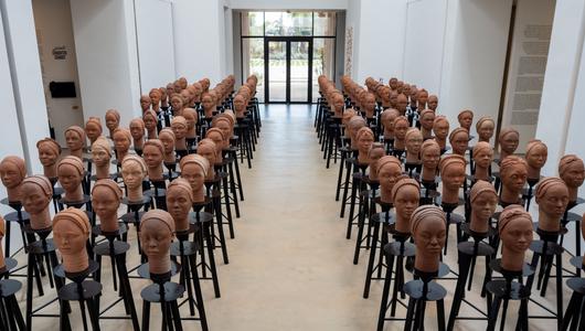 Clay sculptures of heads are arranged in rows in a gallery.