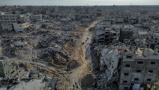 An aerial view of destroyed buildings with people walking among the rubble.