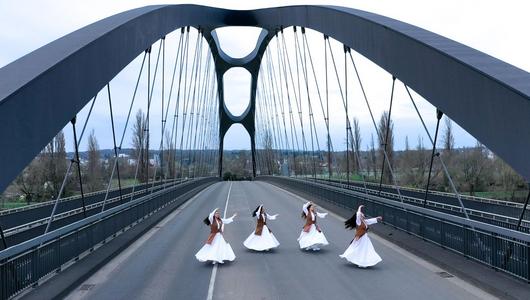 Auf einer bogenförmigen Autobahnbrücke tanzen vier Frauen in weißen Gewändern und langen dunklen Haaren.